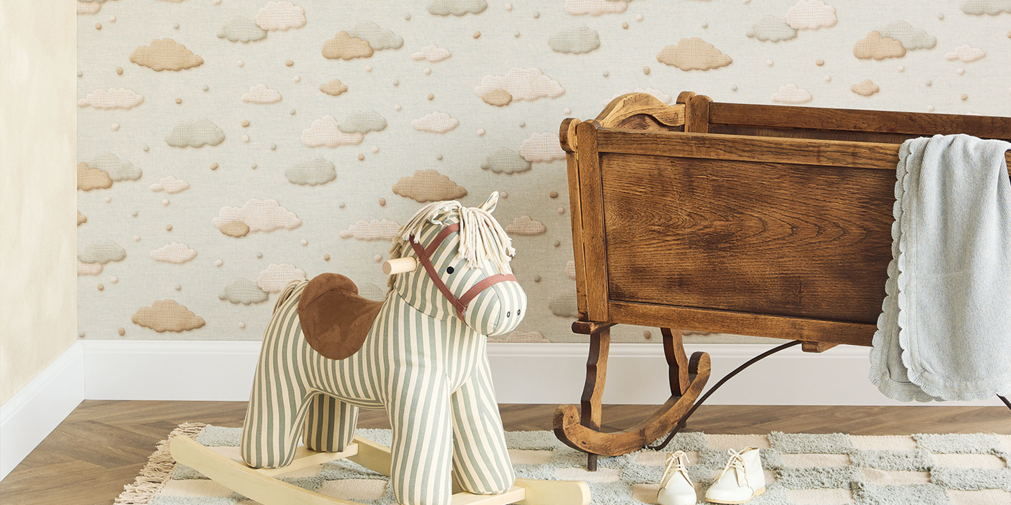 Kinderzimmer mit Kindertapete mit Wolken Muster in Beige und Blau und nostalgischem Schaukelpferd neben Holz Wiege