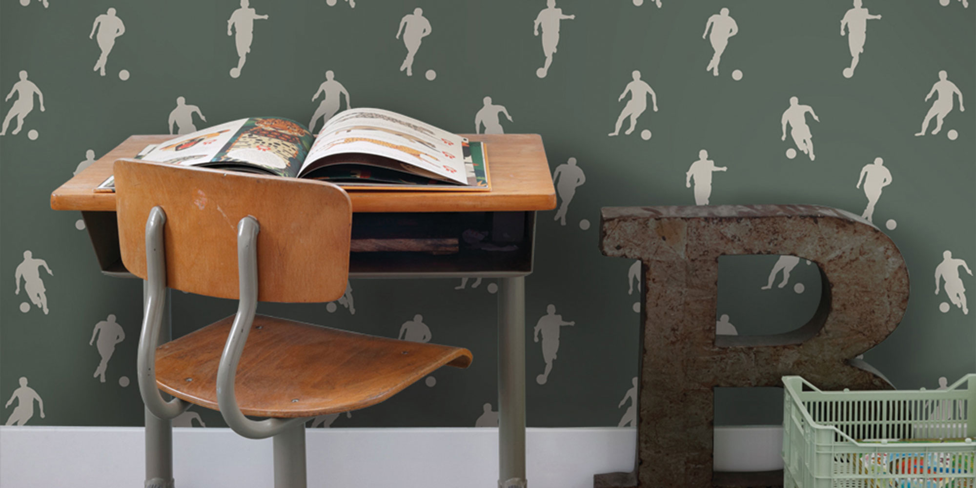 Grüne Fußballtapete im Kinderzimmer mit weißen Fußballmotiven, Schreibtisch und Buch als sportliche Wandgestaltung für kleine Fußballfans
