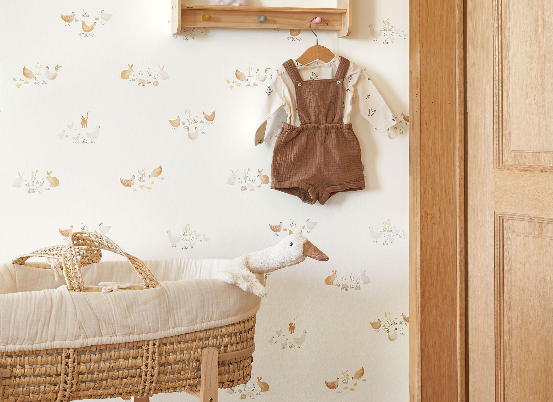 Natürliches Babyzimmer mit heller Tiertapete mit Hühnern, Hasen und Katzen sowie geflochtenem Babykorb
