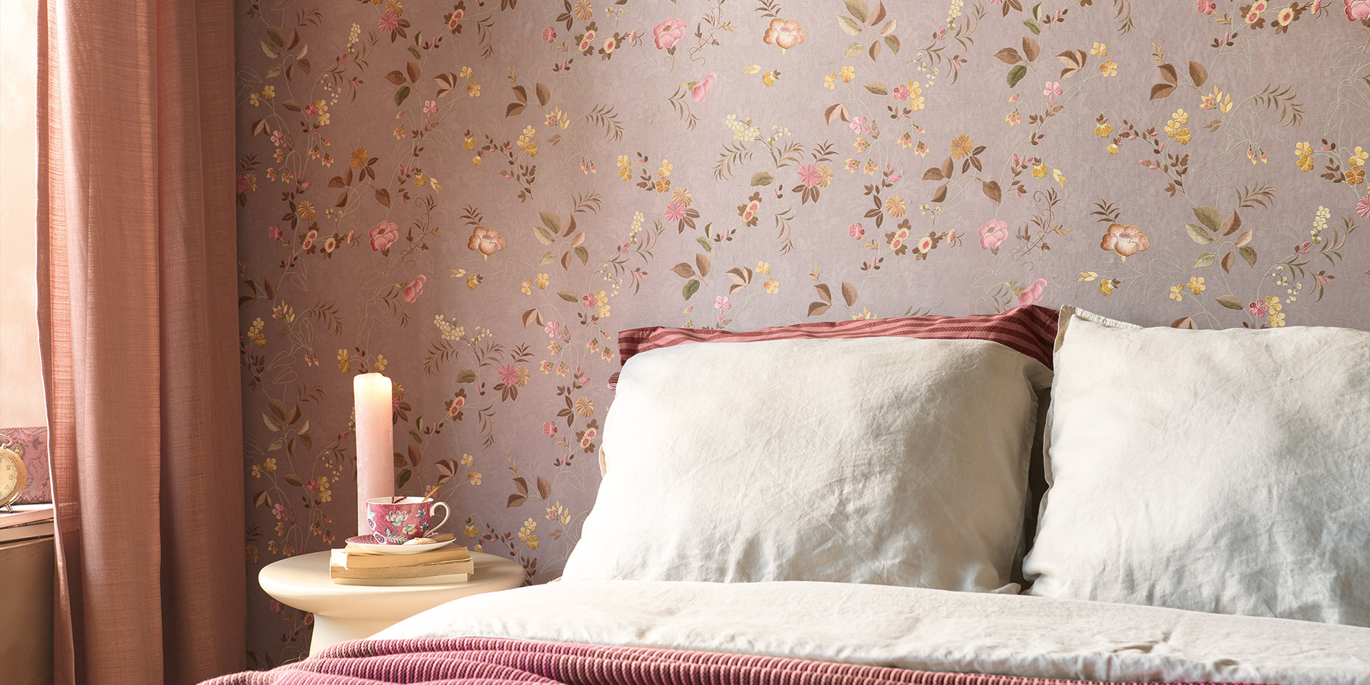 Gemütliches Schlafzimmer mit einer romantischen Blumentapete in Beige- und Rosatönen. Weiche Textilien und eine warme Beleuchtung runden das Ambiente ab.