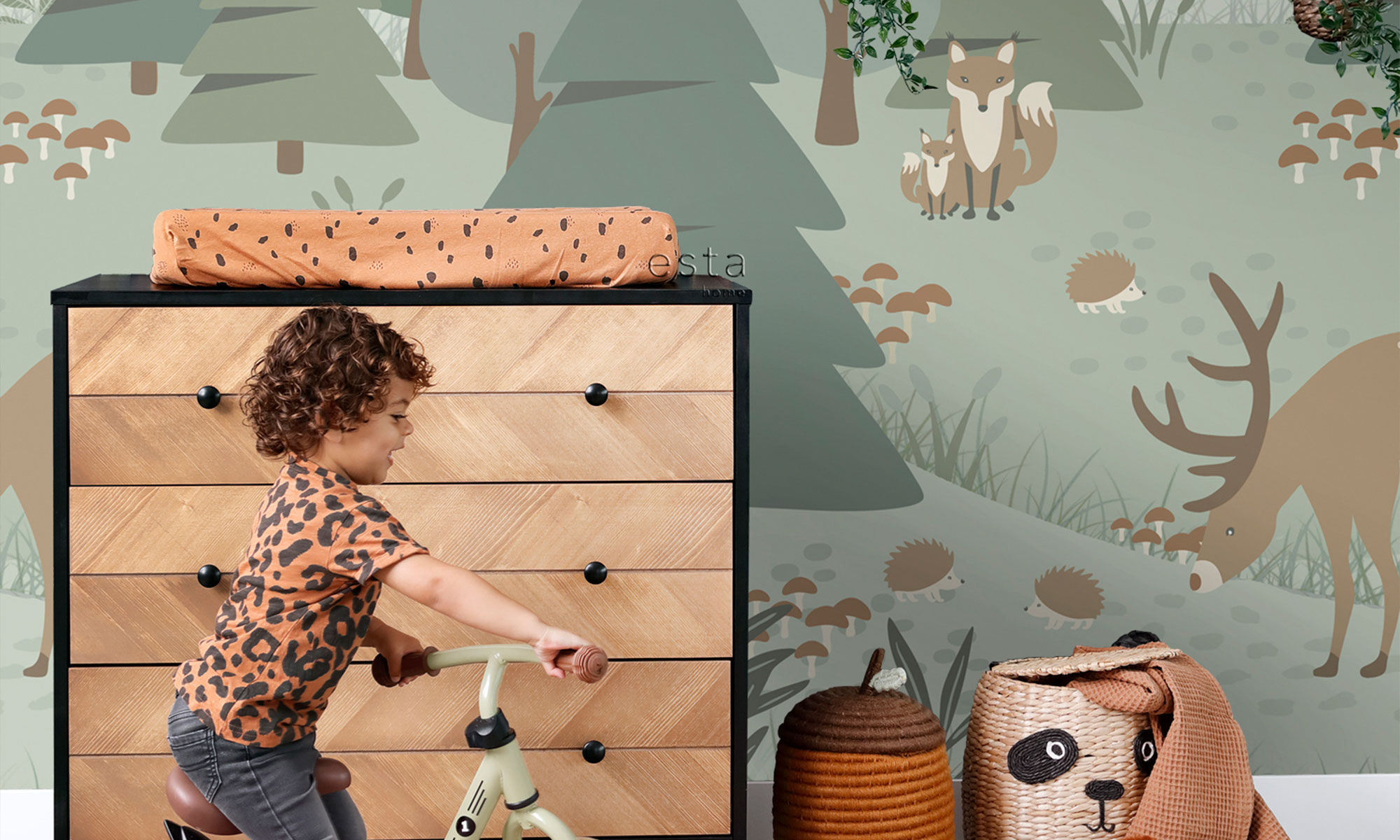 Kinderzimmer mit grünem Wald-Wandbild mit Fuchs, Reh, Igeln und Pilzen sowie spielendem Kind