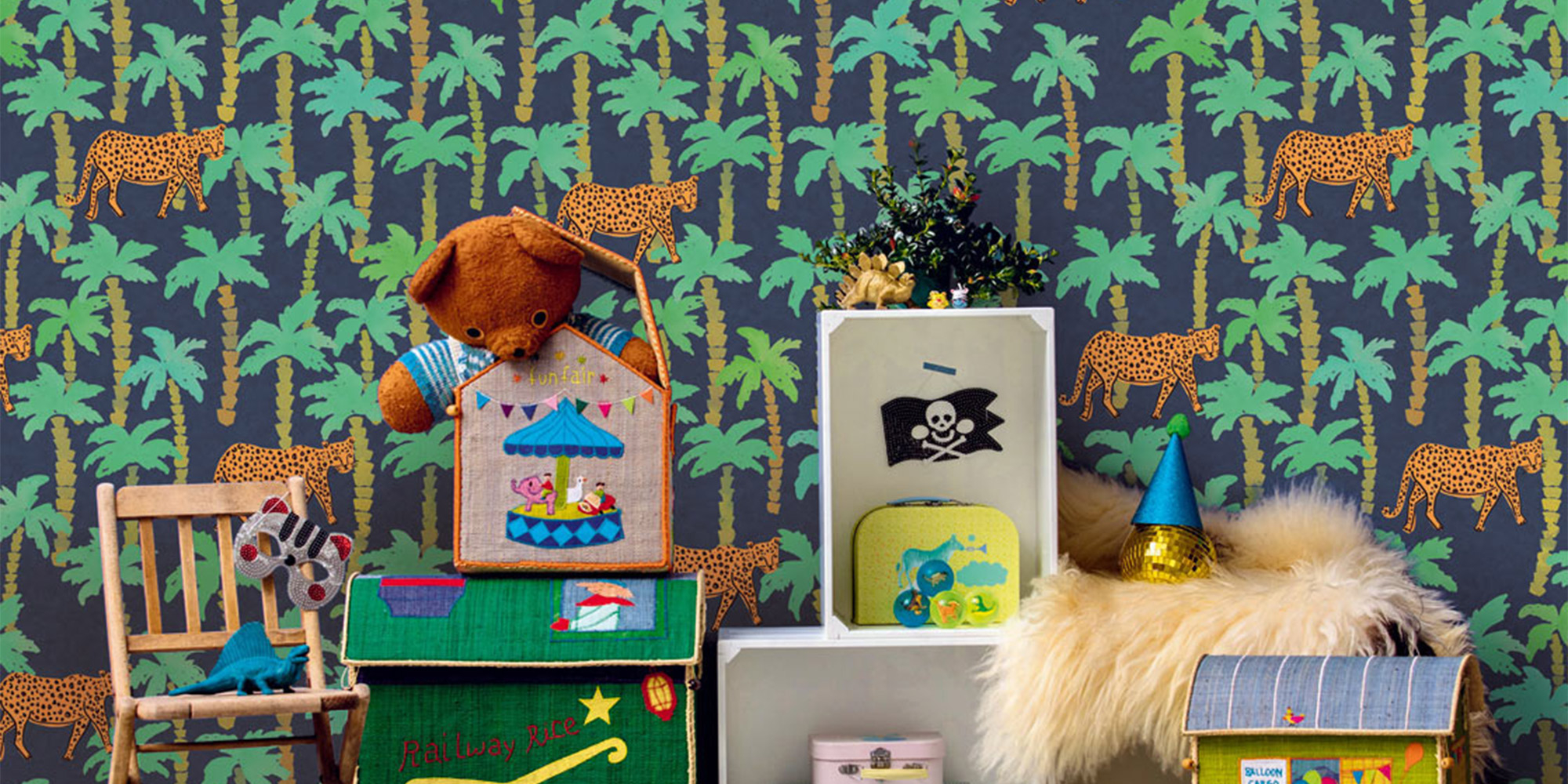 Wandgestaltung in der Spielecke eines Kinderzimmers mit einer dunkelblauen Tapete, verziert mit Palmen und Leoparden, die eine exotische Atmosphäre schafft.