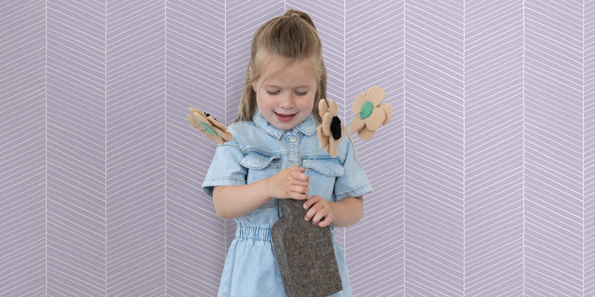 Mädchen mit Blumen bastelt vor einer lila Fischgrät-Tapete im modernen Kinderzimmer