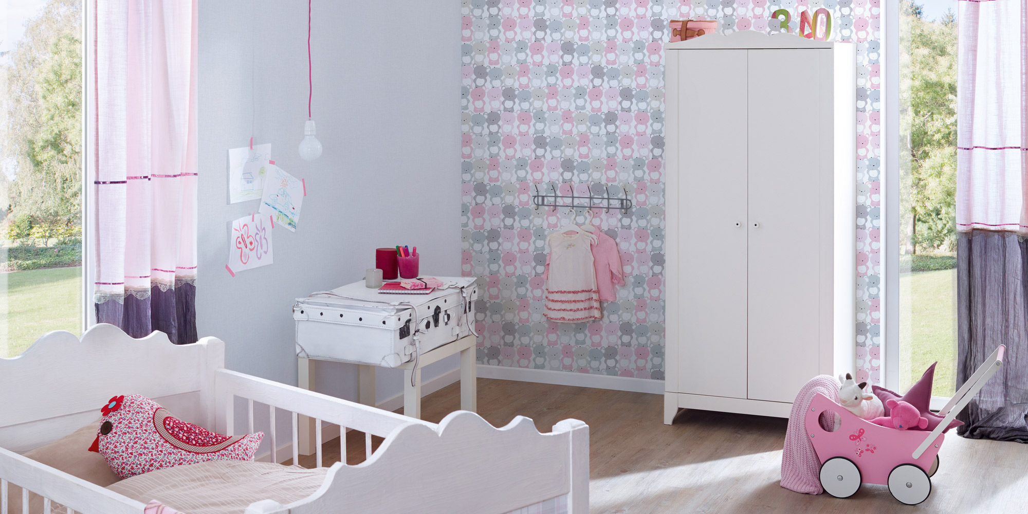 Babyzimmer mit einer Kombination aus grauer Unitapete und einer Kindertapete mit rosa und grauen Bärchen, die eine gemütliche und liebevolle Atmosphäre schafft.