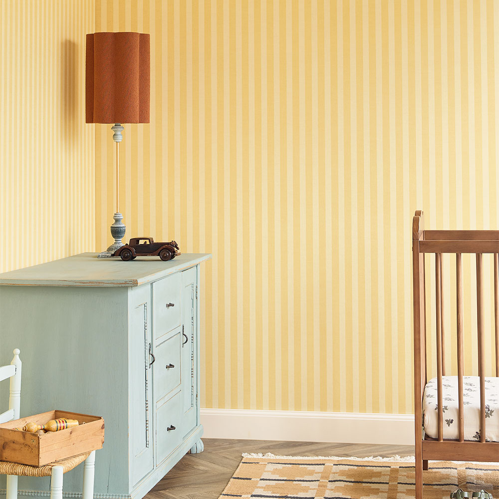 Gelbe Streifentapete im Kinderzimmer mit Kommode, Lampe und Babybett als freundliche Wandgestaltung mit zeitlosem Muster