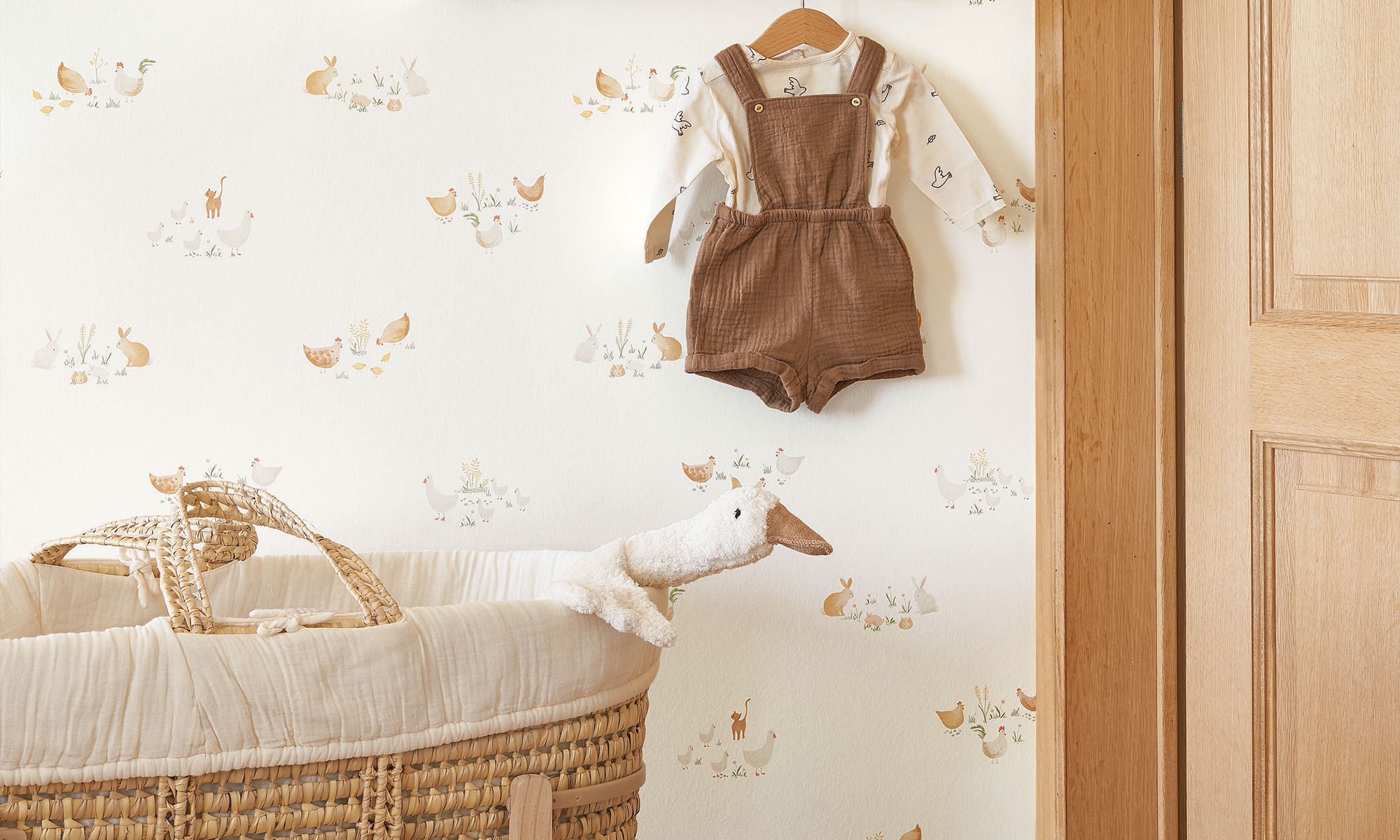 Natural nursery with light animal wallpaper featuring chickens, rabbits and cats, alongside a woven baby basket