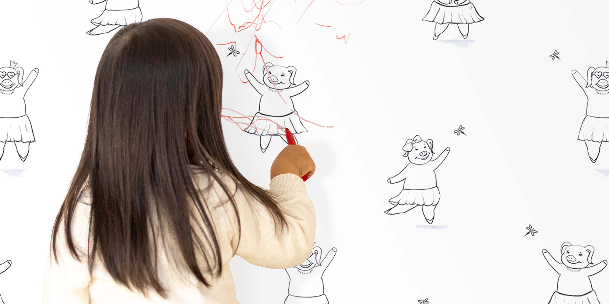 Ein junges Mädchen malt auf einer kreativen Tapete mit niedlichen, tanzenden Schweinchen in Schwarz-Weiß. Die Tapete ist zum Ausmalen gedacht und fördert die Kreativität der Kinder.