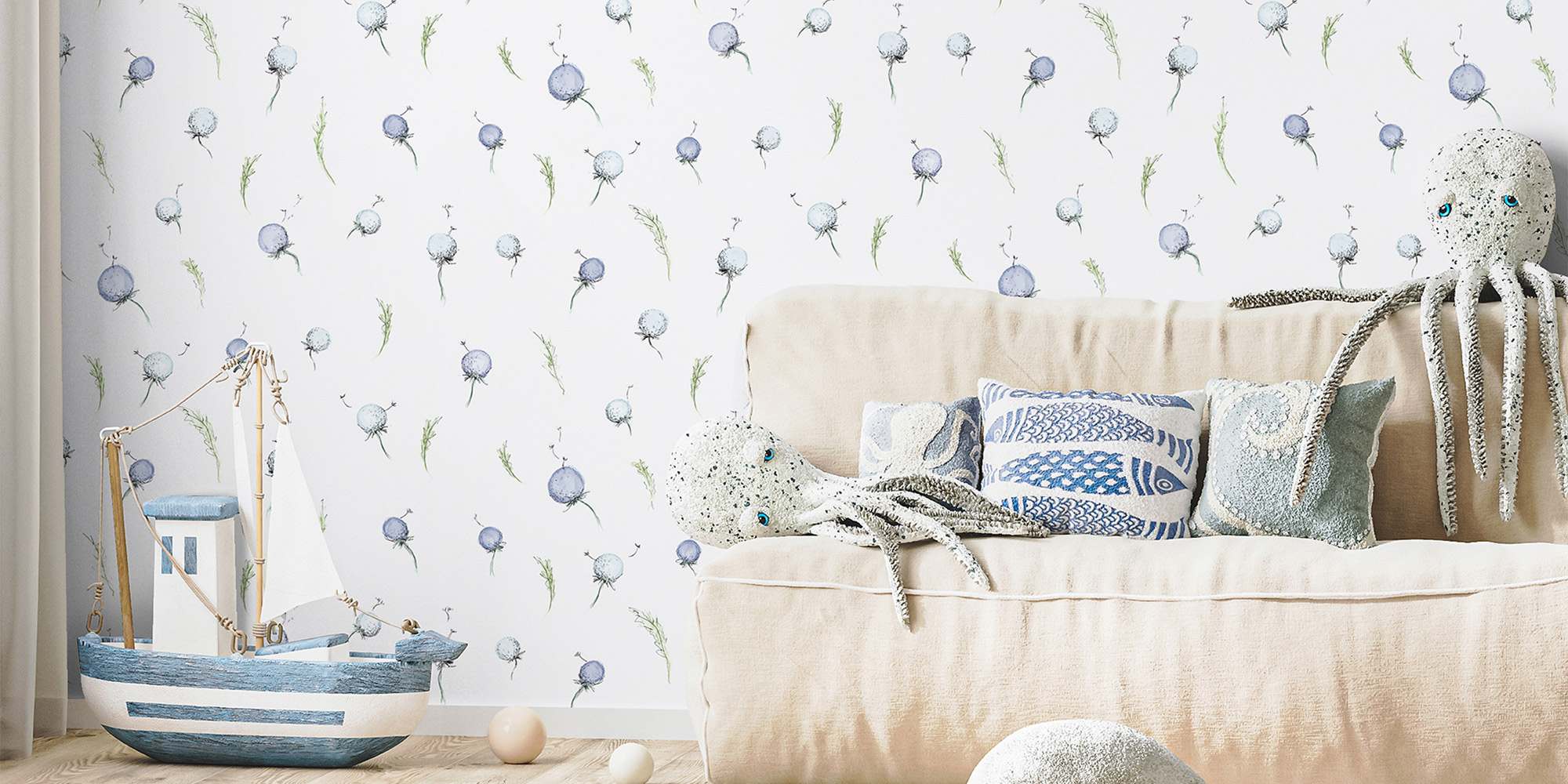 Ein charmantes Kinderzimmer mit maritimem Thema, dekoriert mit einer zarten blauen Tapete mit schwebenden, löwenzahnähnlichen Blumen. Kuschelige Oktopus-Spielzeuge und ein hölzernes Segelboot vervollständigen den Küsten-Look.