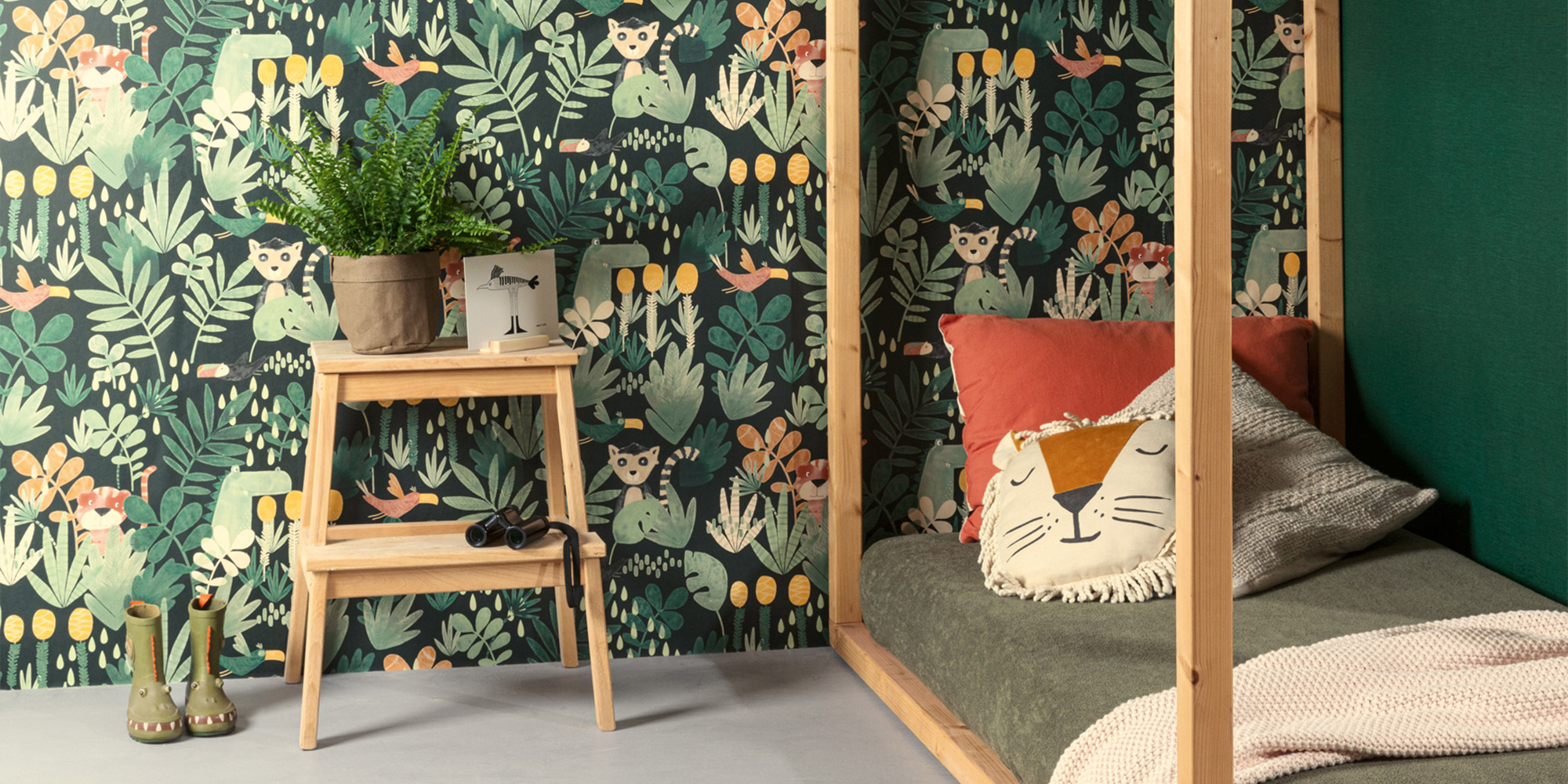 Gemütliches Kinderzimmer mit dunkler Tapete im Dschungel-Stil, mit Lemuren, Pflanzen und tropischen Elementen. Ein Holzhausbett mit Kissen und Pflanzen vervollständigt das Ambiente.