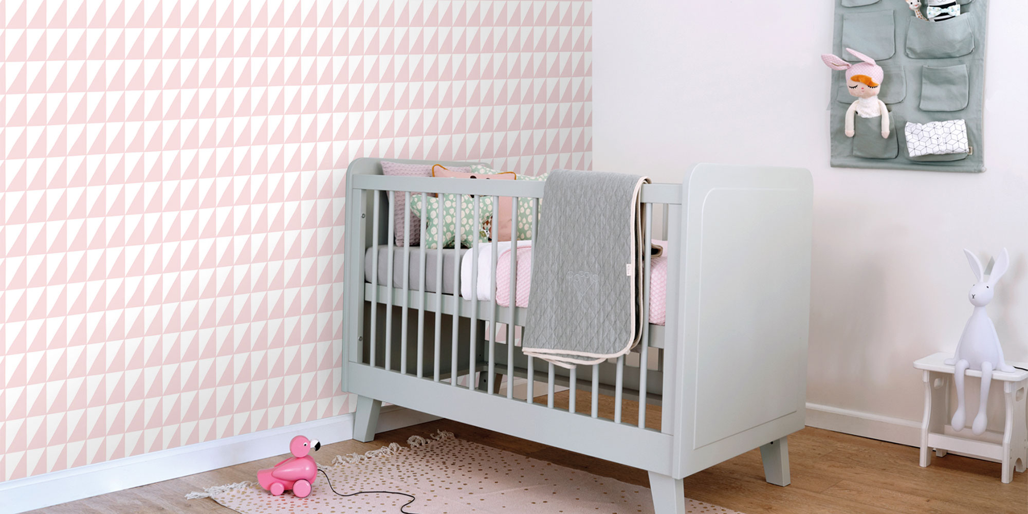 Babyzimmer mit rosa Dreiecke Kindertapete im geometrischen Muster neben grauem Babybett