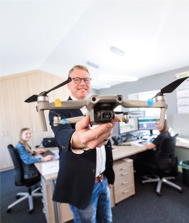 Dirkt Ewering steht in einem modernen Büro und zeigt eine Drohne. Dirk Ewering geht mit der Zeit und zeigt eine moderne Drohne als Beispiel für die modernen und digital ausgestatteten Büros.