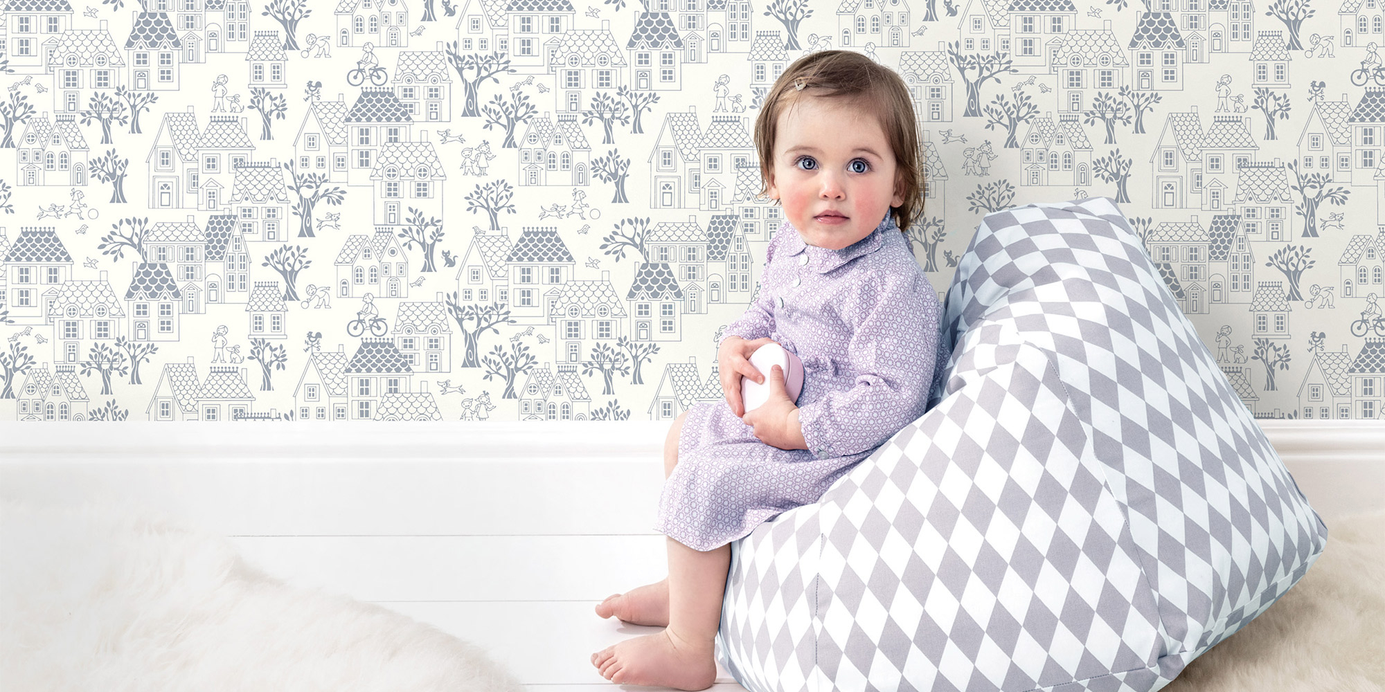 Grau-weiße Kindertapete mit gezeichneten Häusern und Bäumen, kombiniert mit einer eleganten weißen Fußleiste aus Stuck.